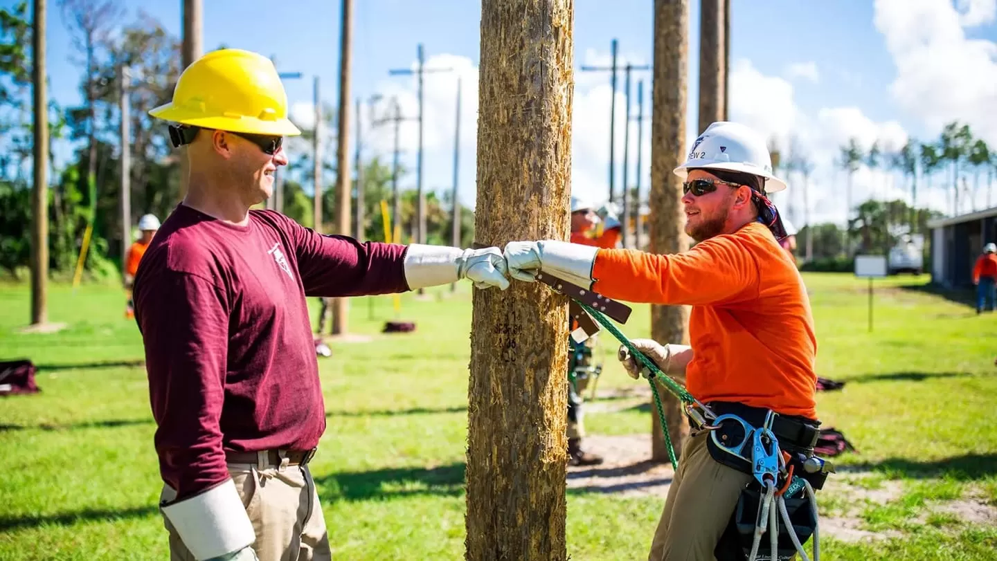 2 linemen fist bumping in front of a tree